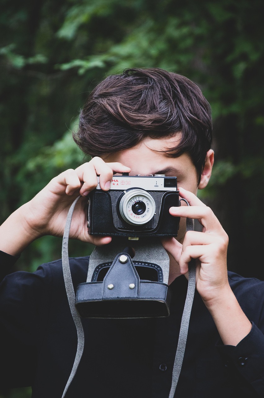 a boy holding a camera to take a photo facing to the camera man